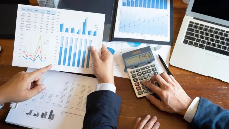 Business people looking at pharmacy performance in front of paperwork, laptop and calculator